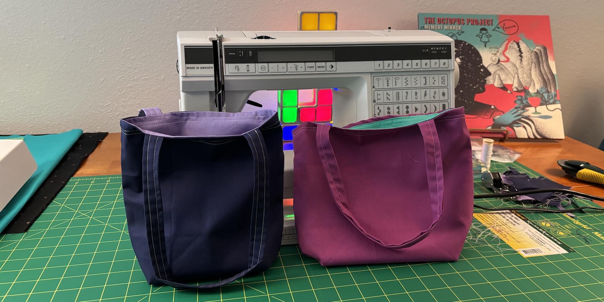 Two finished fat quarter totes sitting on my craft table in front of my sewing machine. The left is clearly better made, and the right was clearly made first.